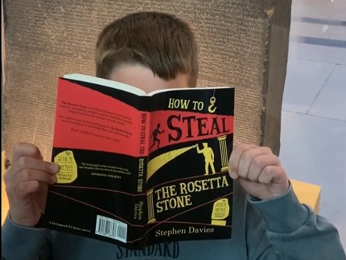 A boy reading a heist novel in front of the Rosetta Stone